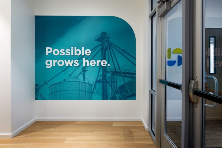 An wall-size image of a grain elevator overlayed with blue reads, "Possible grows here" near the doors of the Scoular employee entrance.