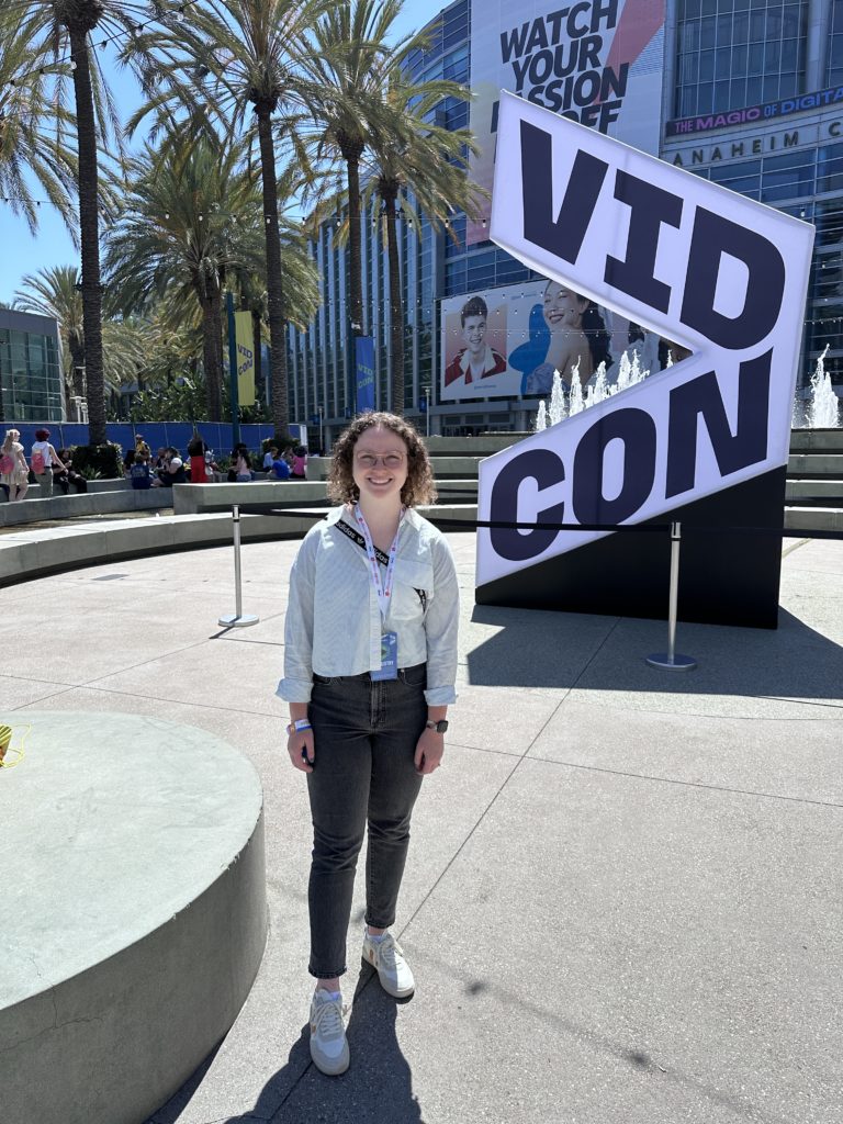 Abbie Perry, E&S Strategist, stands outside in front of the large VidCon sign.