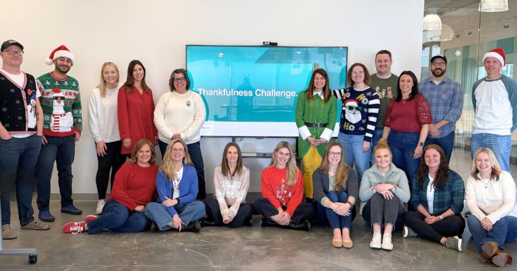 Group photo of smiling E&S employees posing in front of a screen that says "Thankfulness Challenge 2024"