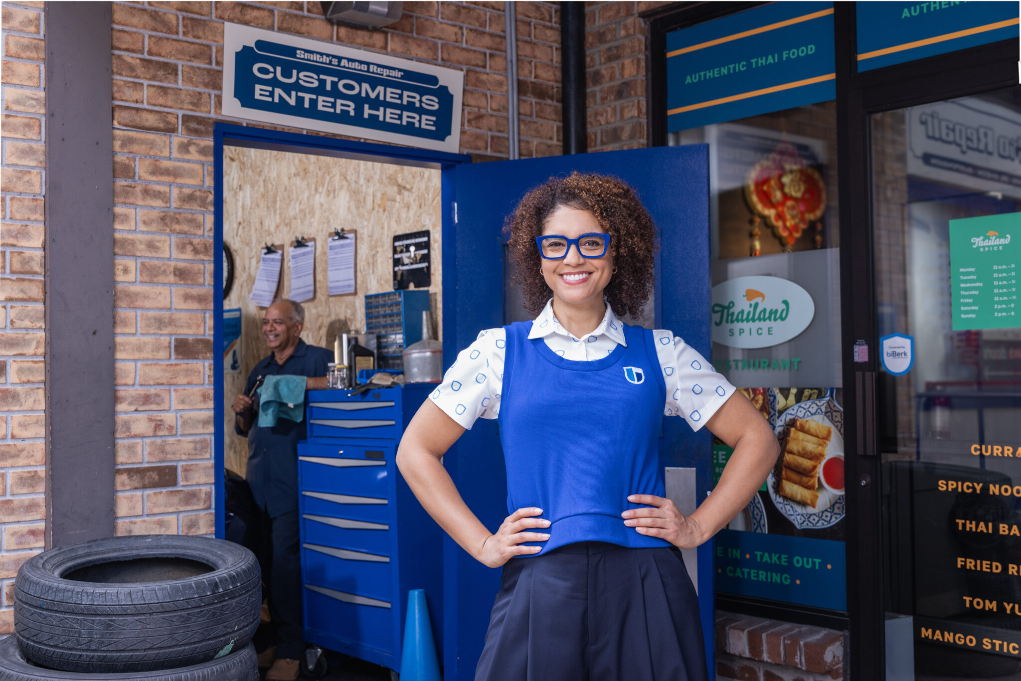 Berklyn, biBerk's spokesperson, smiling confidently with hand on her hips, standing in front of a strip mall with a mechanic and Thai restaurant.