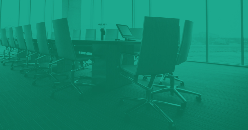 Teal image of a boardroom. There are office chairs around a large table.