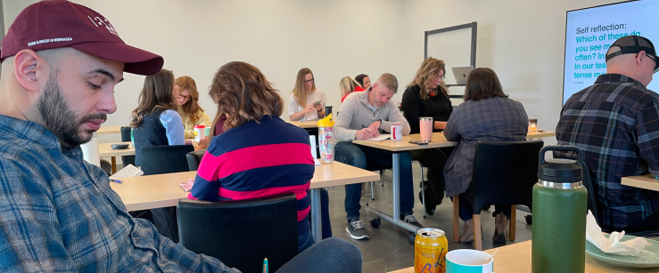 E&S team members sit in small groups in a conference room, writing notes in their notebooks