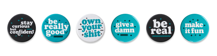 Six metal buttons display Ervin & Smith’s values: Stay curious but confident, Be really good, Own your shit, Give a damn, Be real and Make it fun.